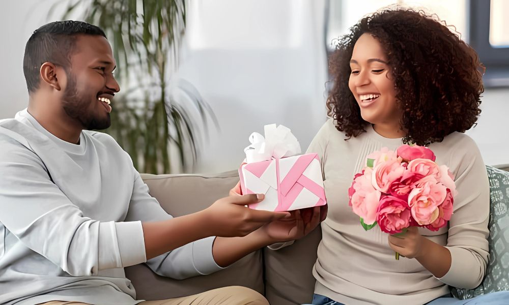 Smiling couple exchanging a wrapped present and flowers representing the Receiving Gifts love language