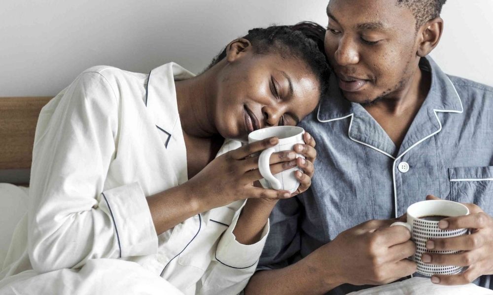 Couple sitting together in pajamas, holding coffee mugs and cuddling, showing love and affection in a healthy relationship